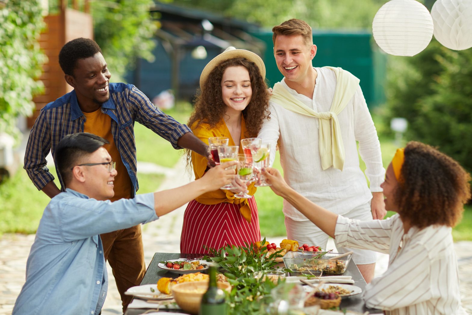 A diverse group of adults toast at a picnic table in an outdoor space.